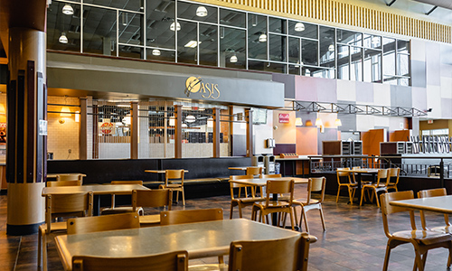 A photo of the dining area of Oasis, with empty chairs and tables. The Oasis logo is displayed on a wall.