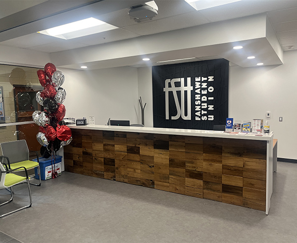 A photo of the front desk of the FSU office. AN FSU logo is shown on the wall. Red and silver balloons are present in a corner.