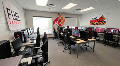 Modern esports gaming room with multiple high-end PCs and ergonomic chairs arranged in rows, featuring Fuel Esports branding on walls.