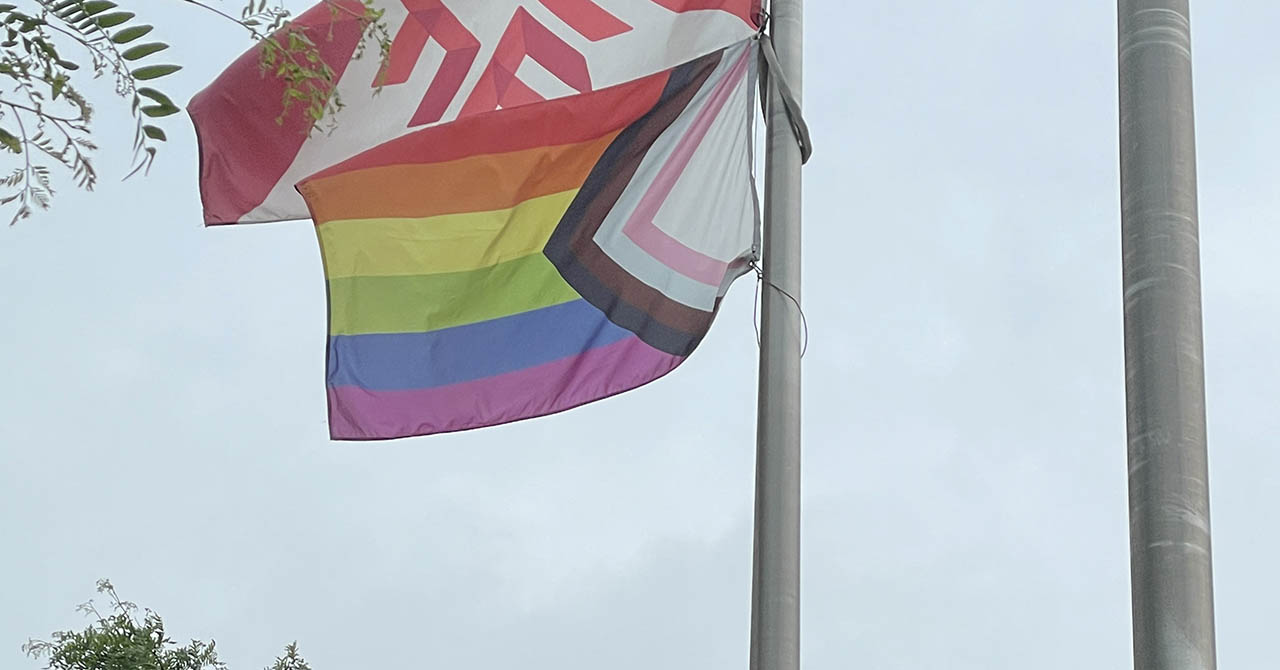 A Progress Pride flag and Fanshawe College flag hanging on flag poles.
