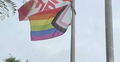 A Progress Pride flag and Fanshawe College flag hanging on flag poles.