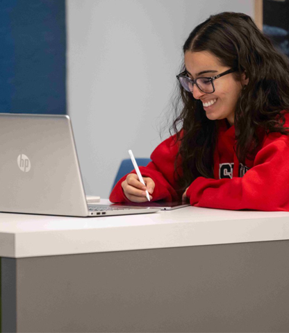 A young person smiling while working on a laptop.