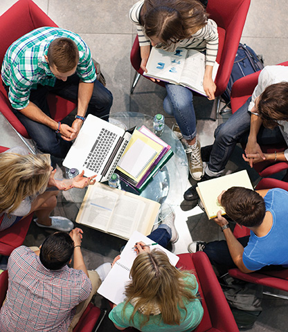 An overhead shot of five people with laptops and notes on paper