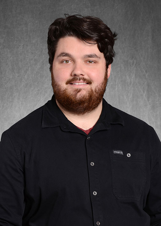 A headshot of Douglas Peters smiling, standing in front of a grey background.