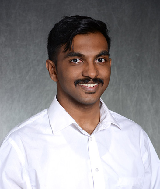 A headshot of Stephin Sathya smiling standing in front of a grey background.